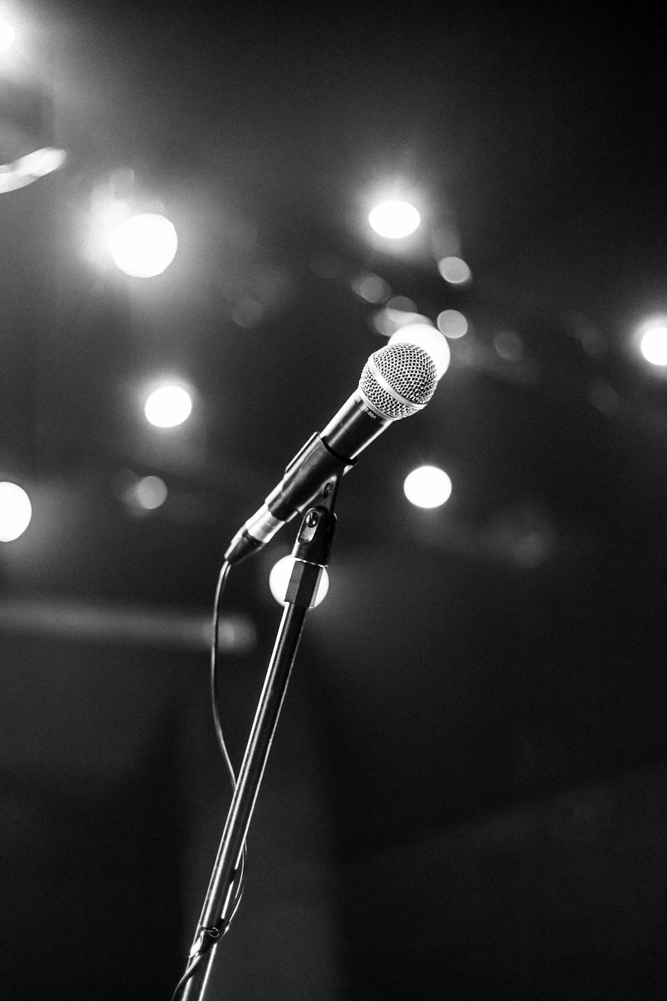 A black and white image of a microphone on a stage, spotlight highlighting its presence.