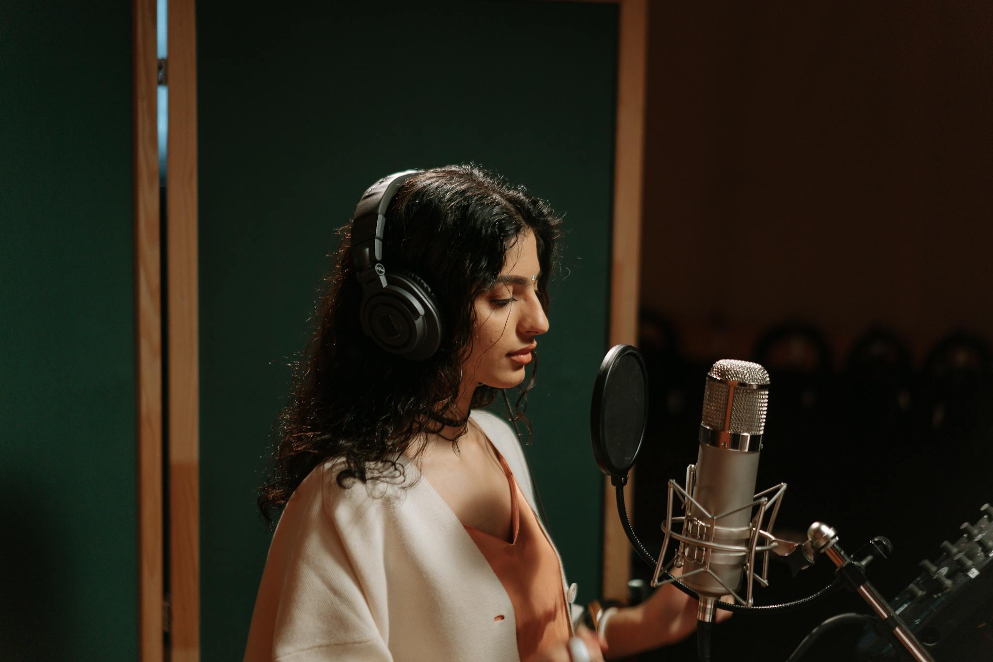 A female singer recording vocals in a professional music studio with a microphone.