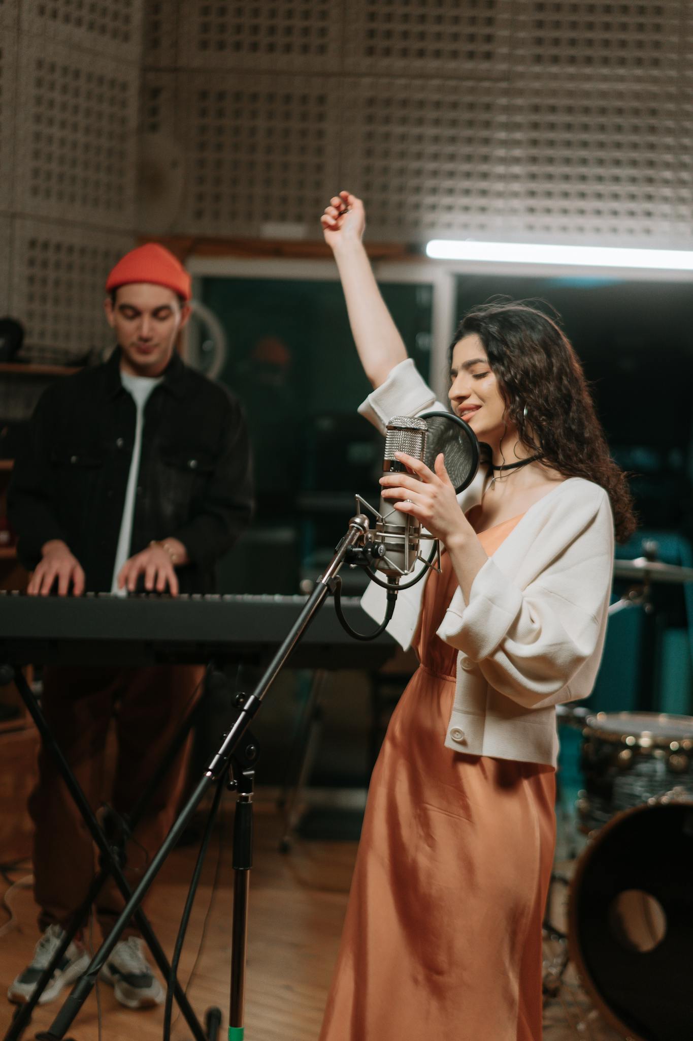 Energetic woman singing with keyboard accompaniment in a music studio.